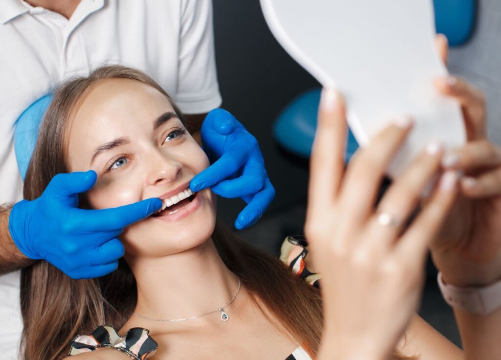 Woman checking her smile in a mirror after professional teeth whitening treatment at a Beverly Hills dental clinic