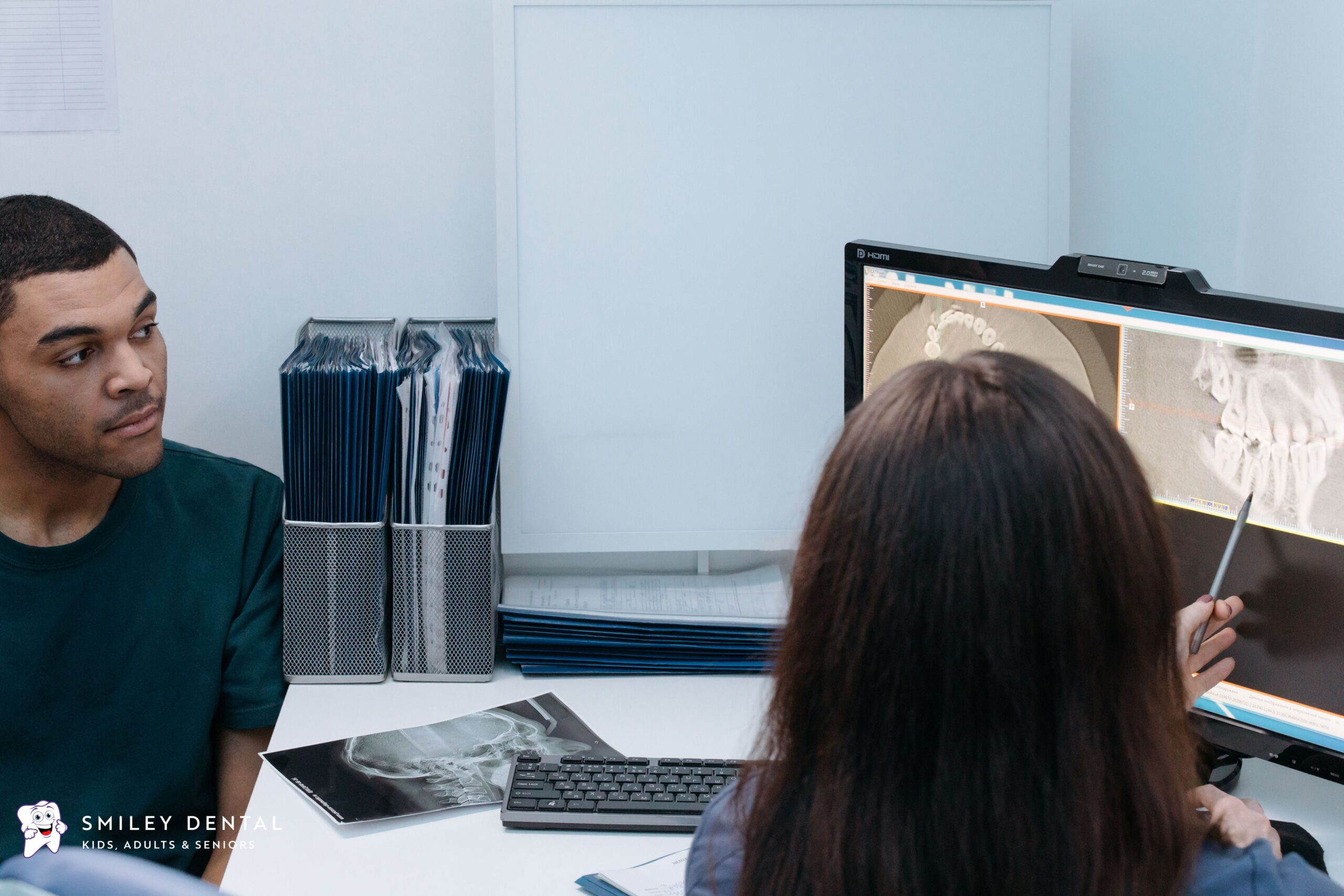 Dentist reviewing dental X-rays with an adult patient during an orthodontic consultation to compare Invisalign and traditional metal braces.