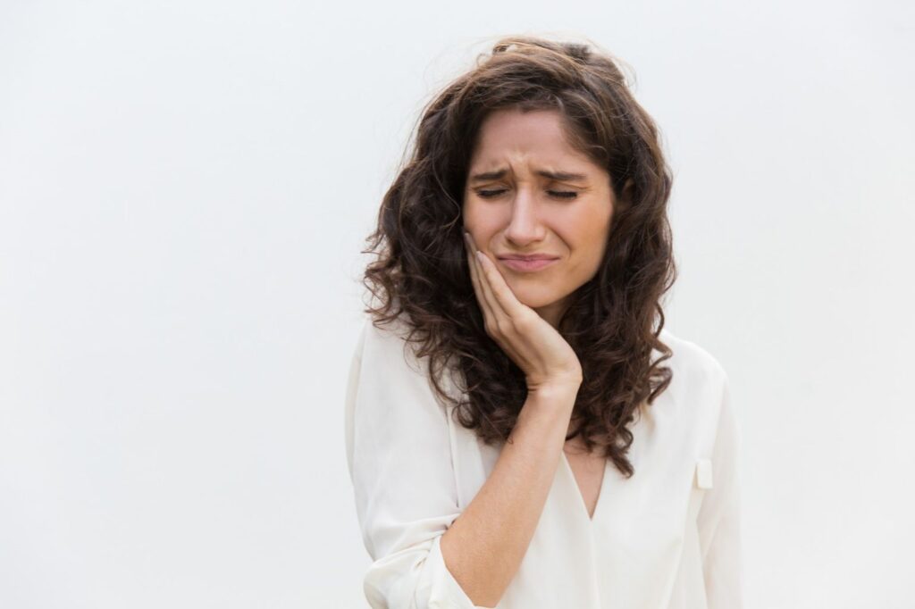 Woman holding her cheek in discomfort from sudden tooth pain